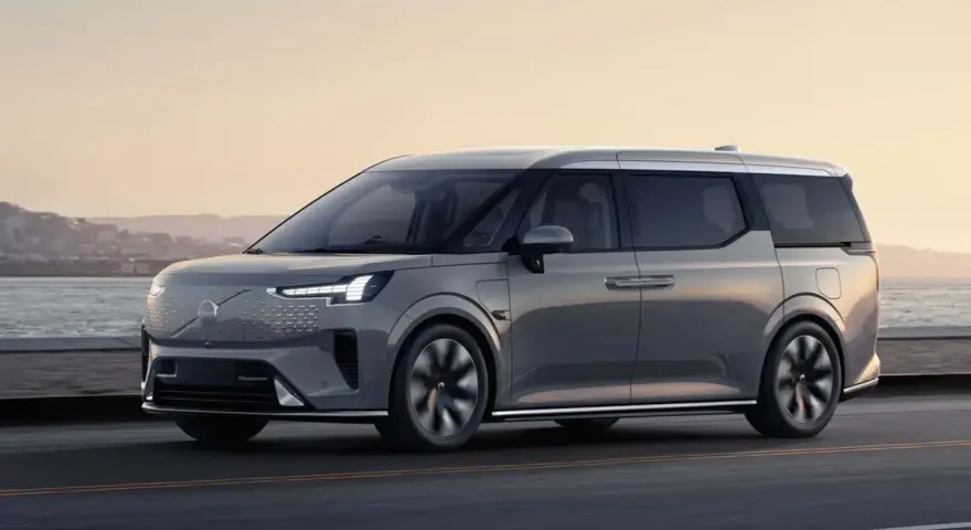Szary luksusowy van elektryczny Volvo EM90 w ruchu drogowym nad morzem.