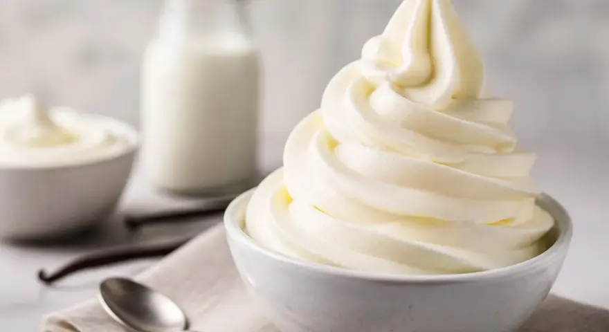 Cremiges Softeis in einer Schüssel, daneben Milch, Vanilleschoten und Löffel. Die Zutaten für das perfekte Softeis.