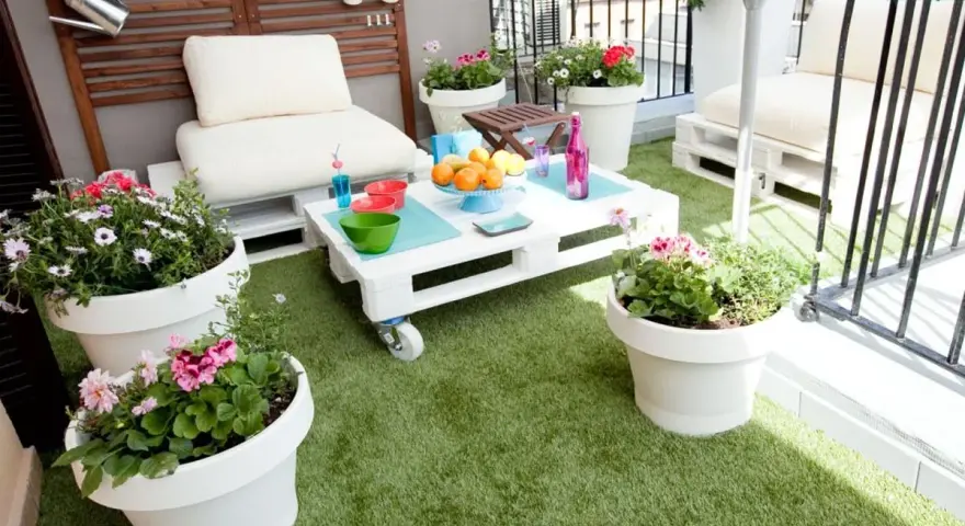 Balcón acogedor con césped artificial, muebles de palets y macetas con flores. ¡Ideas para terrazas con césped artificial!
