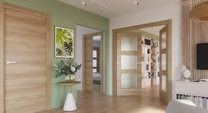 Un pasillo con paredes verde menta y puertas de roble. Un cuadro de hojas tropicales y un jarrón con flores adornan la pared.
