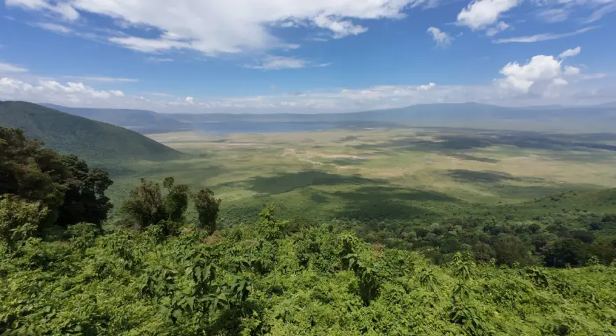 Rozległy widok na krater Ngorongoro z bujną zielenią na pierwszym planie i jeziorem w oddali.