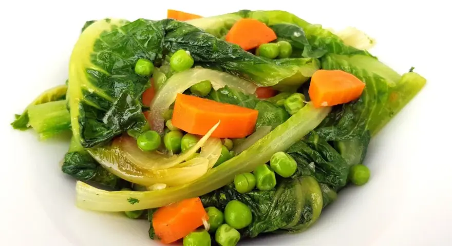 Un assortiment coloré de légumes verts feuillus, de pois et de carottes en dés, rappelant une jardinière de légumes fraîchement préparée.
