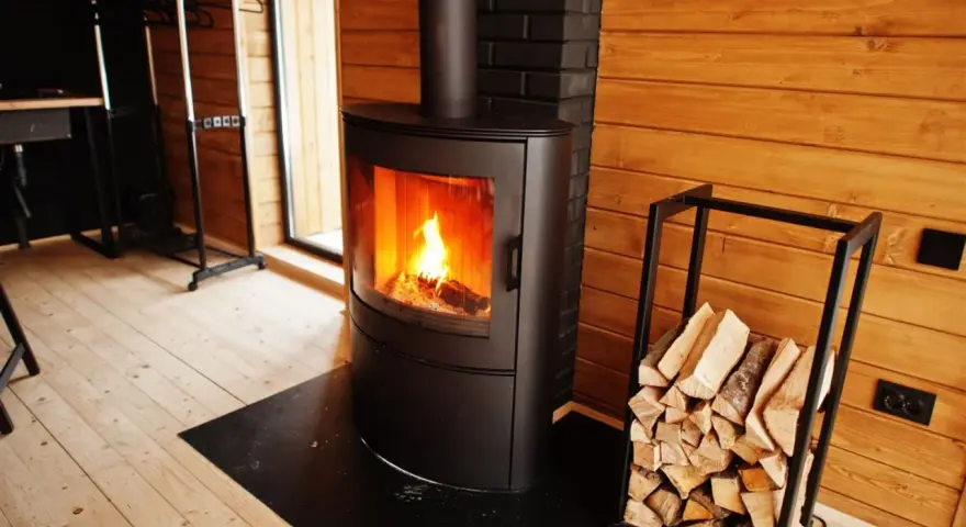 Estufas de leña canalizables modernas con fuego encendido y leña apilada, creando un ambiente acogedor en una cabaña de madera.