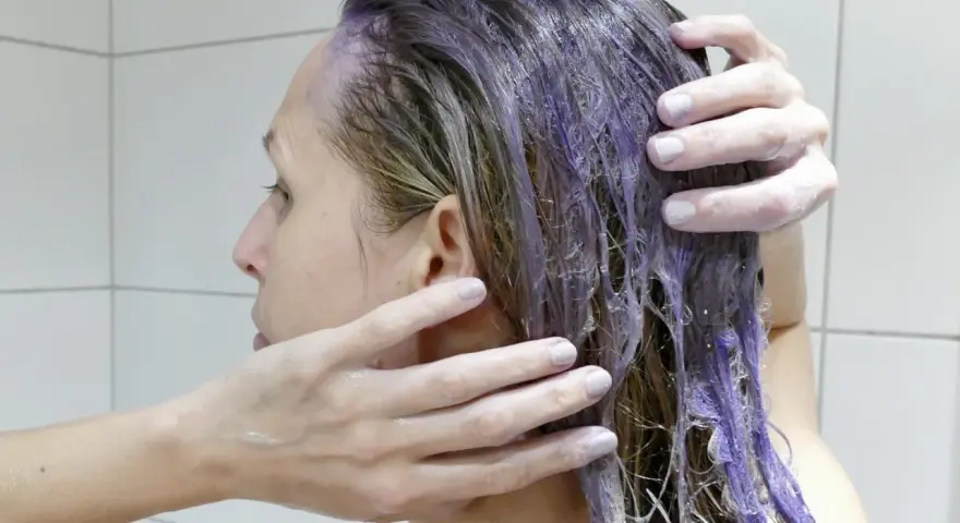 En person masserar in silverschampo med blå pigment i sitt blonda hår.