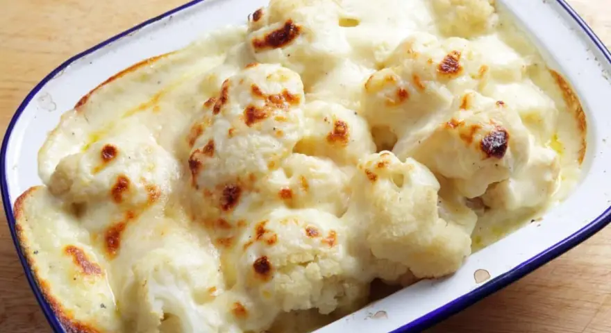 Coliflor gratinada con bechamel cremosa, dorada y burbujeante en una fuente.