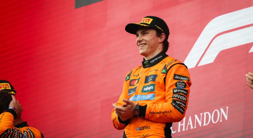 El piloto australiano F1, Oscar Piastri, sonríe en el podio con su mono naranja de McLaren.