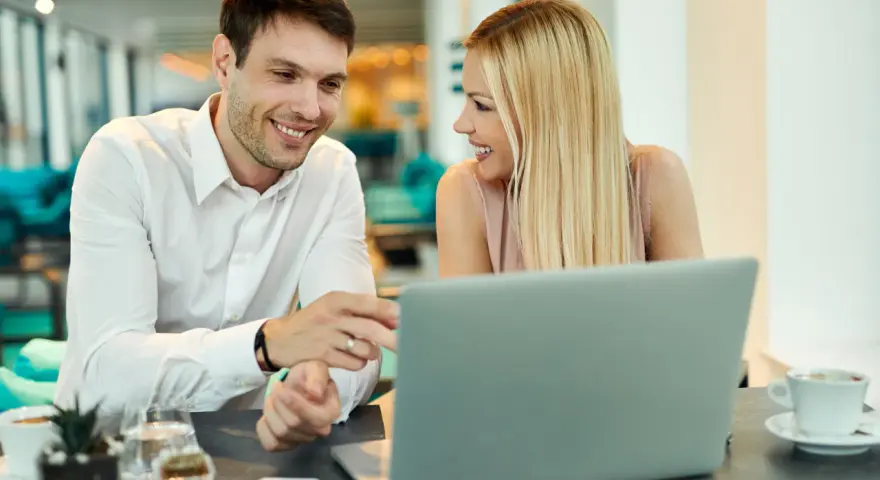 Uśmiechnięci współpracownicy przy laptopie. Ich spojrzenia i gesty sugerują, że to nie tylko praca, ale i rodząca się miłość w pracy.