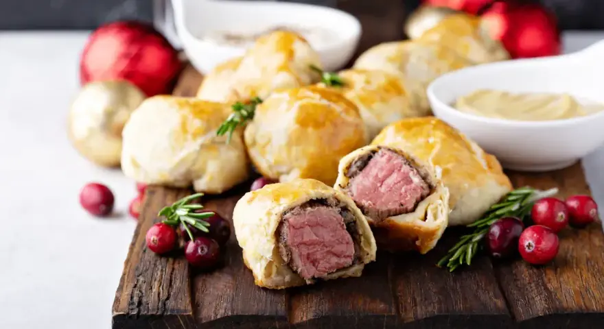 Bouchées à la reine dorées, garnies de viande juteuse, sur une planche en bois avec des canneberges et des décorations festives.
