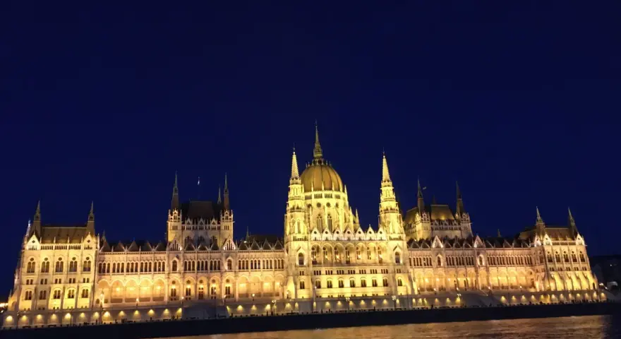 Budynek Parlamentu w Budapeszcie nocą, oświetlony, z odbiciem w Dunaju. Warto sprawdzić ceny na Węgrzech przed podróżą.