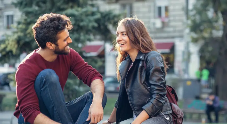 Un homme qui veut vous voir, assis sur l'herbe, rit avec une jeune femme. Ils semblent partager un moment complice et joyeux.
