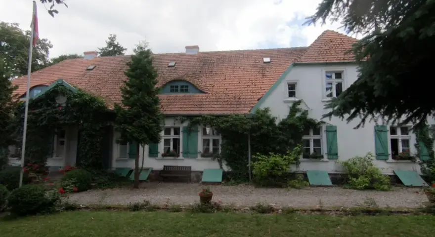 Dwór Wybickich otoczony zielenią, z charakterystycznym dachem i oknami.
