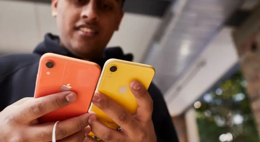 Mężczyzna trzyma dwa telefony: pomarańczowy i **iphone xr żółty**.