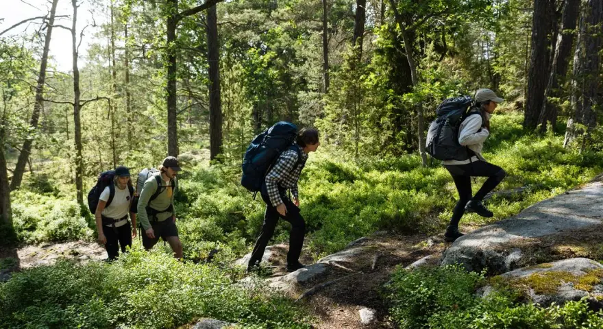 Vandrare med ryggsäckar går uppför en stig i en grön skog. De utforskar olika skåneleden etapper.