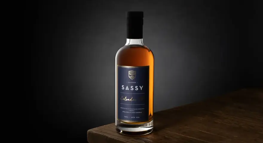 Packshot photo d'une bouteille de Calvados SASSY XO ambré, posée sur une table en bois.