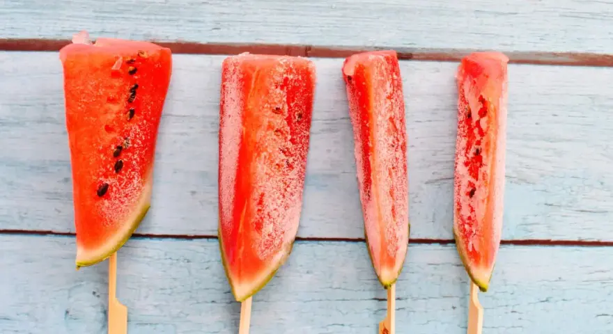Vier gefrorene Wassermelonenstücke auf Stöcken, bereit zum Genießen. Eine erfrischende Idee für Wassermelone einfrieren.