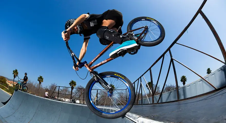 A BMX rider, possibly Chelsea Wolfe, performs a trick on a ramp against a clear blue sky.