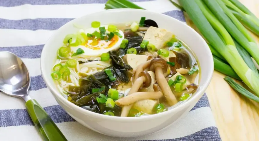 A miska pełna aromatycznej zupy miso z tofu, grzybami, wodorostami, jajkiem i szczypiorkiem.
