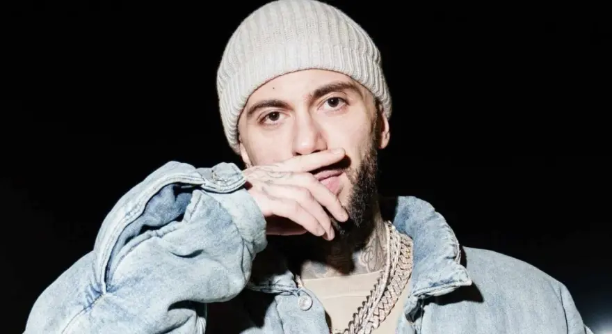 Malik Montana w czapce i jeansowej kurtce, z dłonią na ustach, gotowy na koncert.