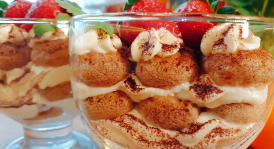 Pyszne tiramisu w pucharkach, przełożone kremem i biszkoptami, ozdobione truskawkami i kakao.