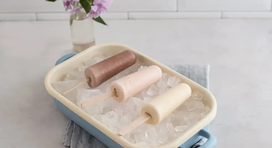 Drei cremige Mini Milk Eis am Stiel, wie aus den 90ern, in einer blauen Schale auf Eiswürfeln.