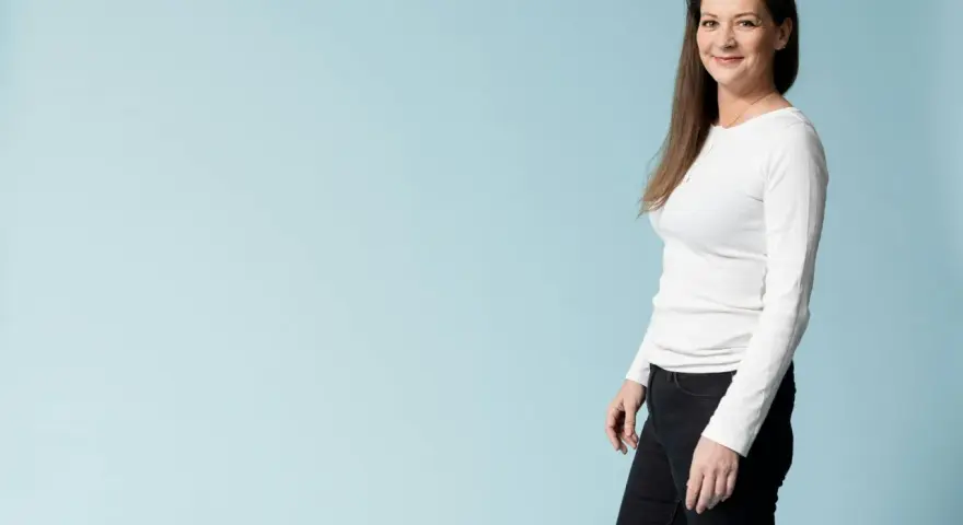 Kvinna i vit tröja och svarta jeans ler mot kameran, redo för en utmaning som fasta 24 timmar.