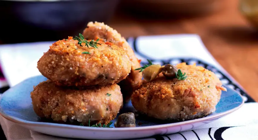 Polpette tonno e patate dorate e croccanti, guarnite con erbe aromatiche e olive, pronte per essere gustate.