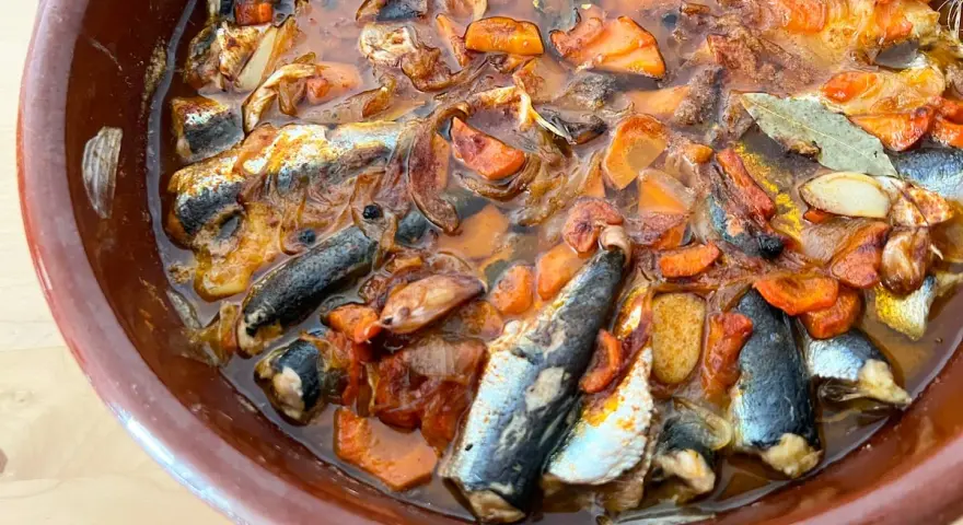 Sardinas en escabeche cocinándose en una cazuela de barro con verduras.