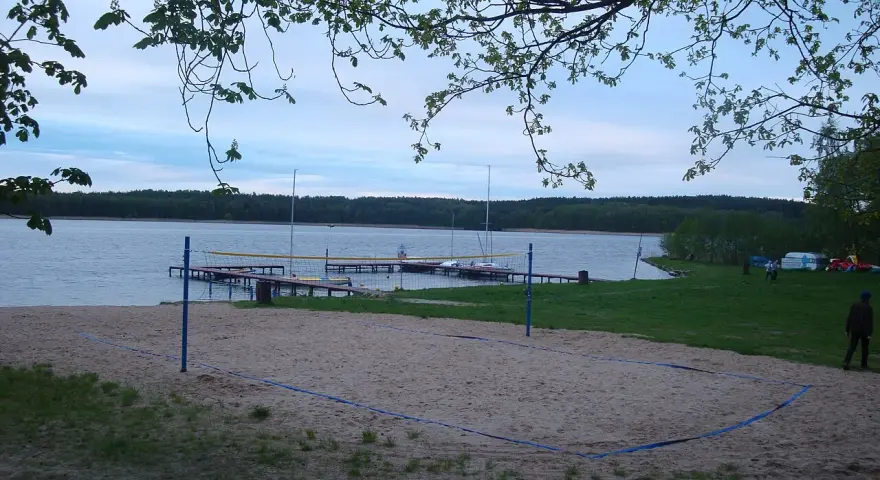 Plaża z boiskiem do siatkówki plażowej nad jeziorem w Borneńskim Sulimowie. W tle pomosty, żaglówki i las.