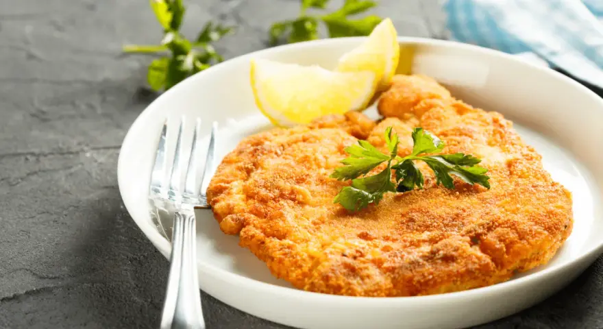 En gyllene schnitzel med citronklyfta och persilja, redo att avnjutas med ett glas vin till schnitzel.