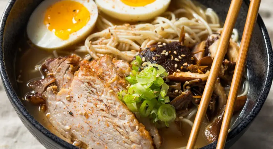 Miseczka aromatycznego ramenu z plastrami wieprzowiny, jajkiem na pół, grzybami i szczypiorkiem. Idealny ramen przepis na rozgrzewający posiłek.