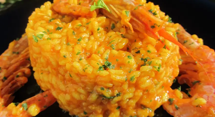 Arroz con gambones, un plato vibrante y delicioso, coronado con gambones jugosos y perejil fresco.