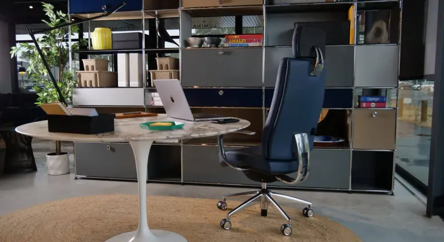 Un fauteuil de bureau design bleu marine, un bureau rond en marbre et un ordinateur portable créent un espace de travail élégant.