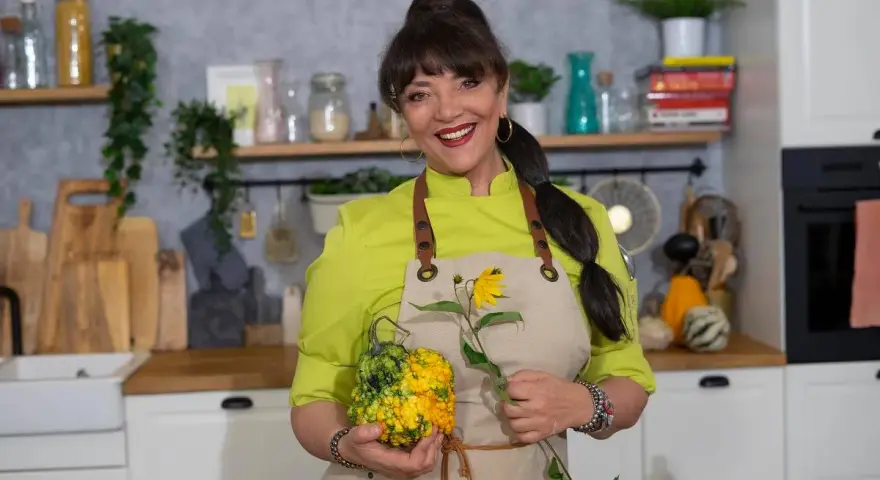 Cristina Catese w kuchni, trzymająca ozdobną dynię i słonecznik.