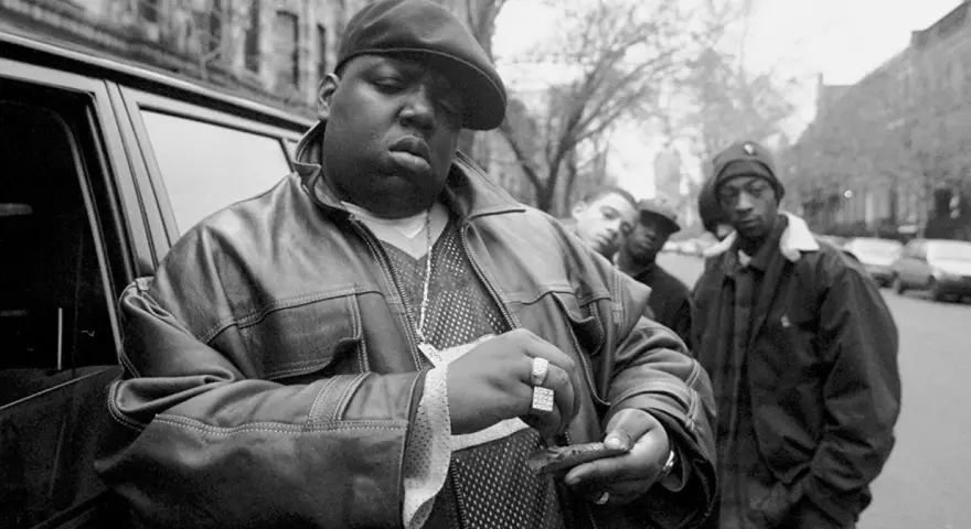 The notorious B.I.G. jak zginął. Raper w skórzanej kurtce i czapce, z towarzyszami, przed samochodem.