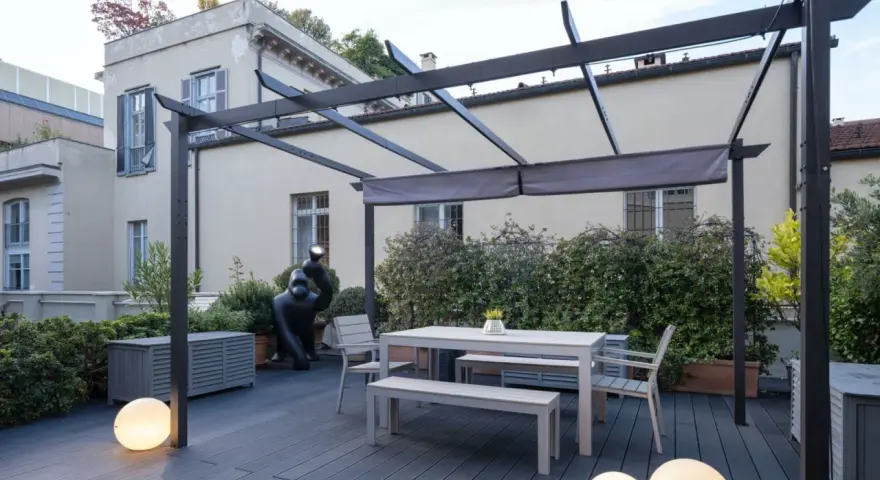 Terrazze arredate con tavolo, panche, sedie e scultura di gorilla sotto una pergola. Illuminazione soffusa con sfere luminose.