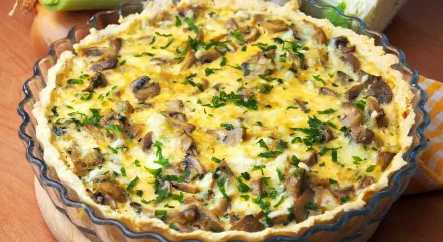 Pyszny quiche z pieczarkami, posypany świeżą natką pietruszki, w szklanej formie.