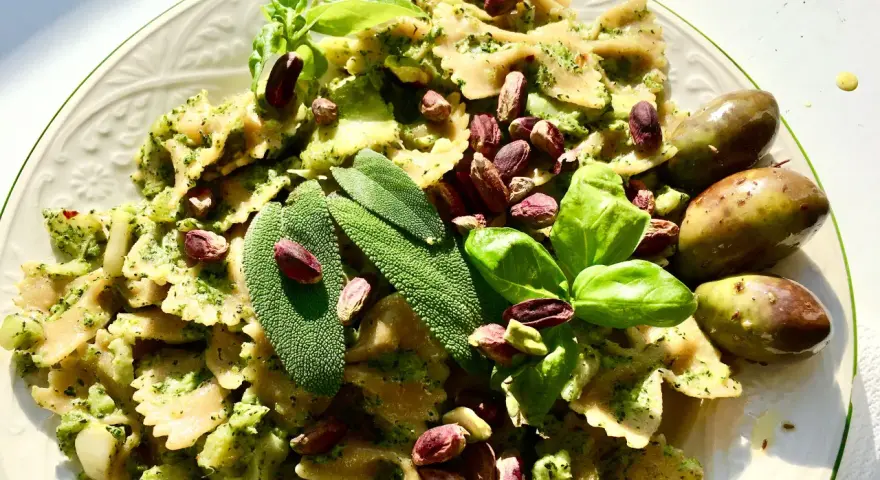 Farfalle condite con un saporito pesto di salvia, guarnite con pistacchi, basilico e olive.