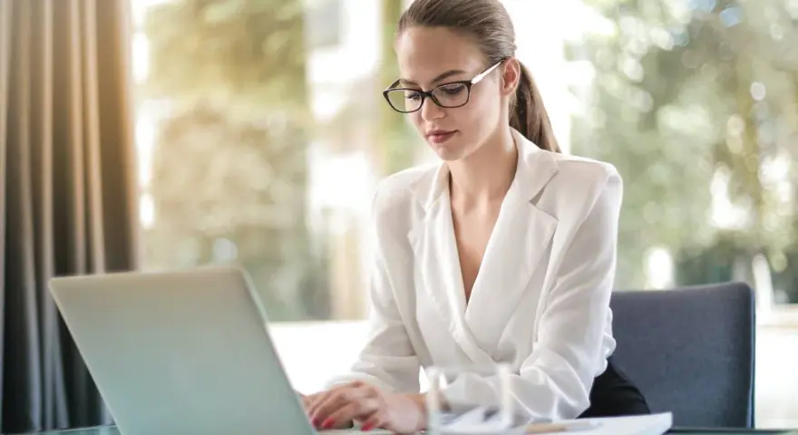 Kobieta w okularach pracuje przy laptopie, zastanawiając się, ile zarabia pracownik banku.