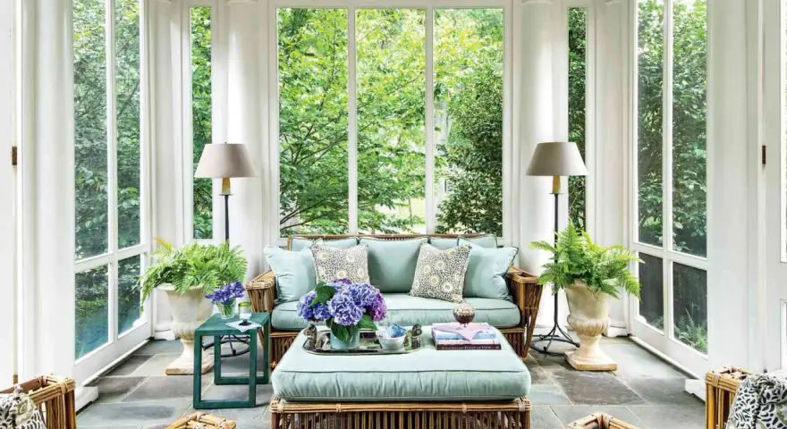 A serene screen porch with rattan furniture, plush cushions, and lush greenery. The natural screen porch materials create a cozy, inviting atmosphere.