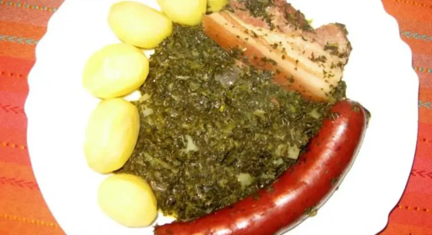 Gedünsteter Grünkohl mit Salzkartoffeln, Kassler und einer herzhaften Lungenwurst, die zum Kochen oder Braten bereit ist.