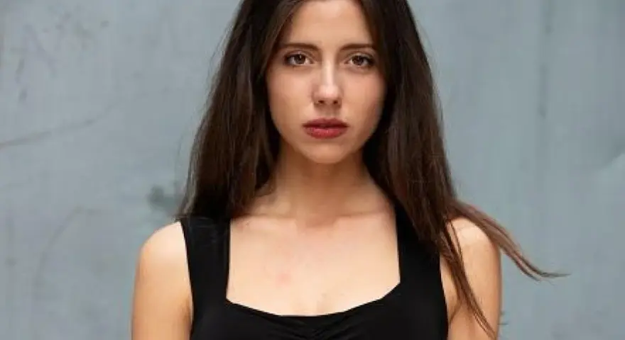 Ritratto di una giovane donna con lunghi capelli castani, indossa un abito nero. Il suo sguardo è intenso, come se stesse aspettando qualcuno, forse celeste dalla porta.