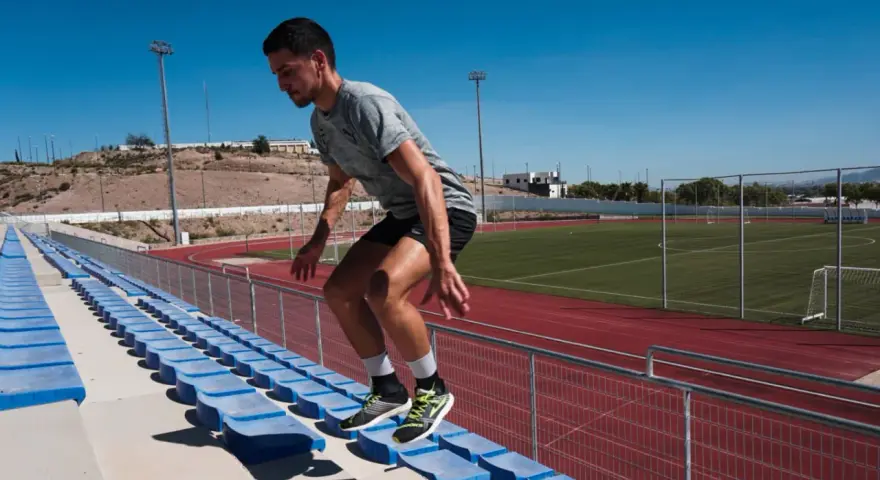 Corredor realiza ejercicios pliométricos subiendo escaleras en un estadio.
