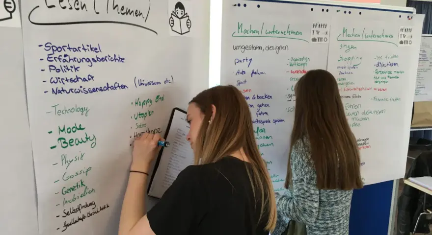 Zwei junge Frauen bei einem Praktikum zur Berufsorientierung, die Ideen auf Whiteboards sammeln.