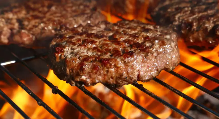 Soczyste kotlety wołowe smażące się na grillu z płomieniami.