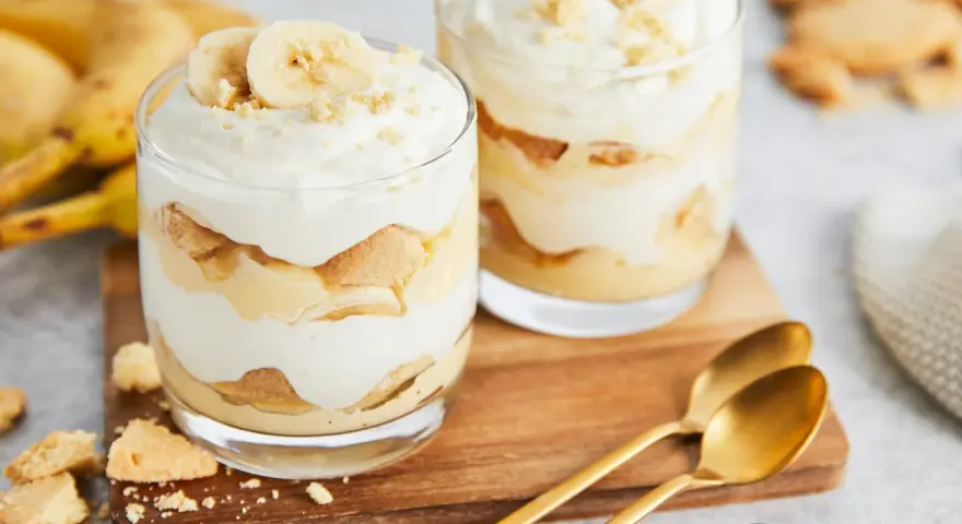 Zwei Gläser mit cremigem Bananenpudding, geschichtet mit Keksen und Bananenscheiben. Ein köstliches Bananenpudding Rezept zum Nachmachen.
