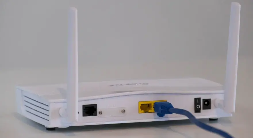 Biały modem z dwiema antenkami, podłączony niebieskim kablem Ethernet. To urządzenie, które pozwala na połączenie z internetem.