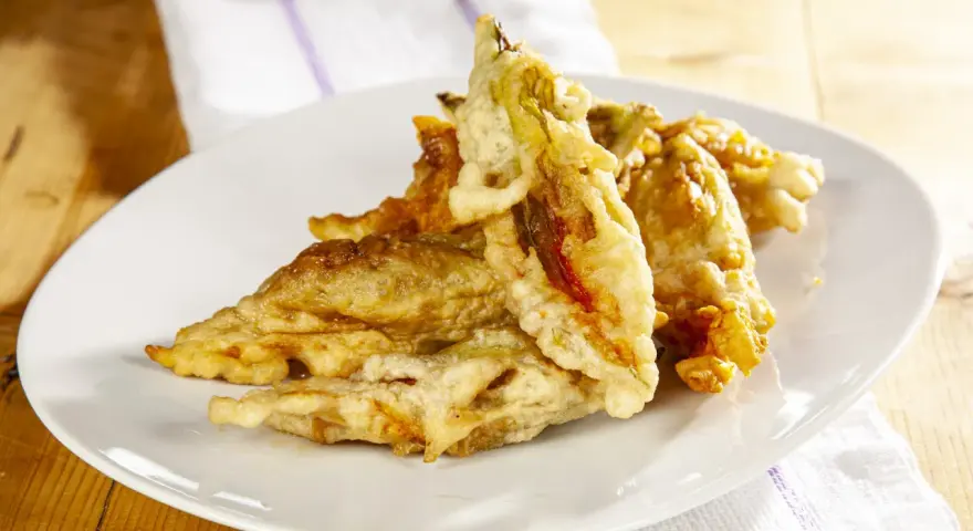 Fiori di zucca fritti dorati e croccanti su un piatto bianco, pronti per essere gustati.