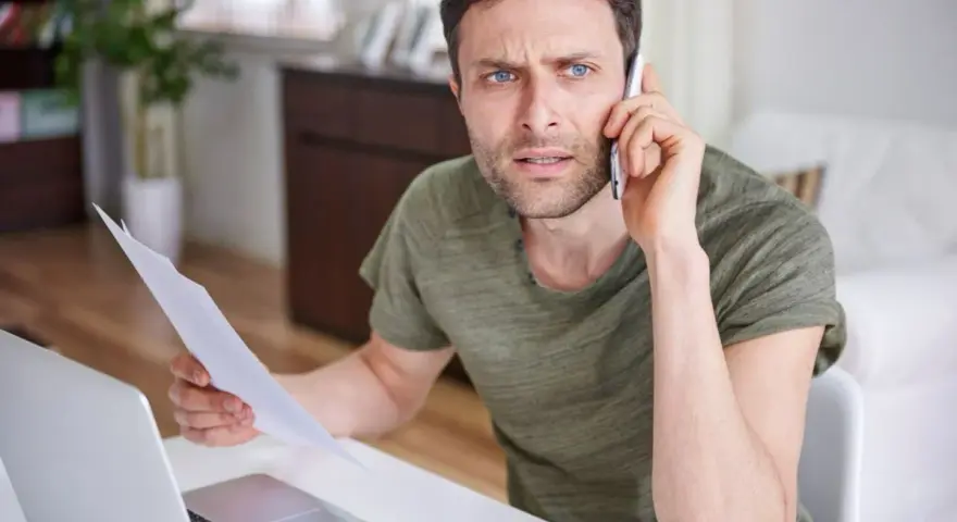Zmartwiony mężczyzna z dokumentami w ręku rozmawia przez telefon, martwiąc się o niespłacony kredyt odnawialny.