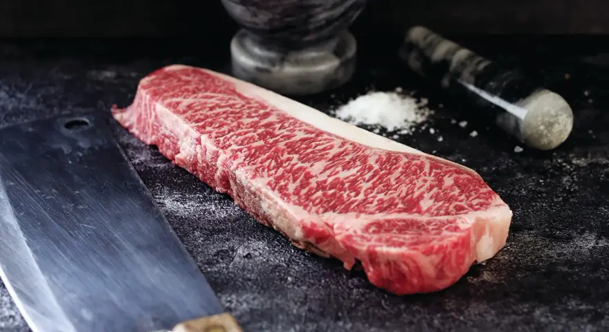 Wyjątkowy stek z krowy wagyu, gotowy do przygotowania. Obok nóż i moździerz z solą.