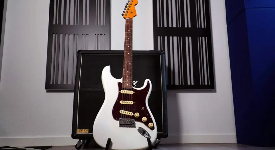 Weiße E-Gitarre mit sechs Saiten steht vor einem Verstärker.